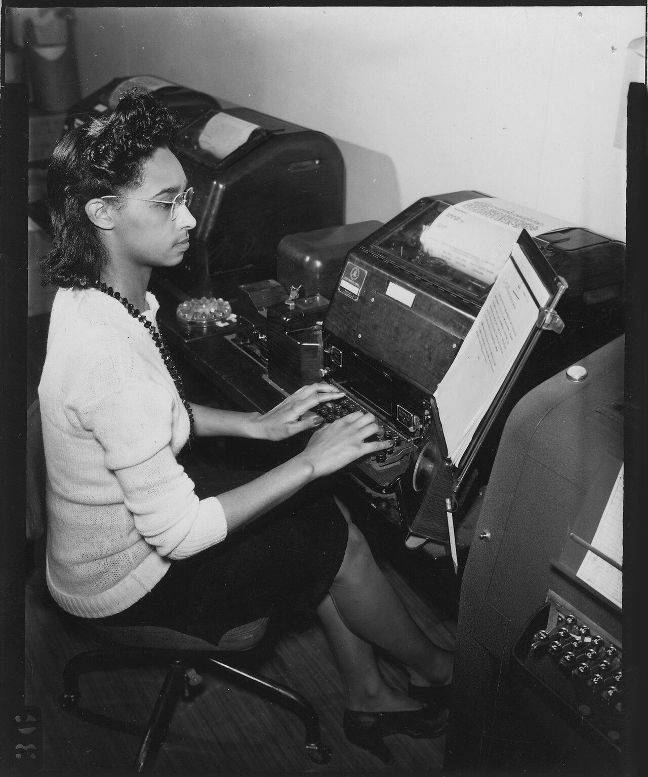 A single teletype machine in a quiet office, paper tape curling onto the floor.
